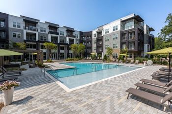 A swimming pool with lounge chairs and umbrellas in front of an apartment building